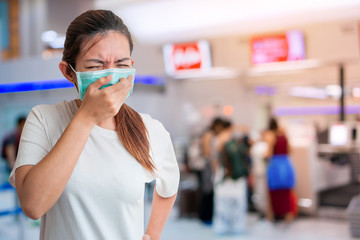 Asian woman coughing and wear medical protective face mask for protect infection the virus and  with blur background of a lot people at airport, Global healthcare and infection concept