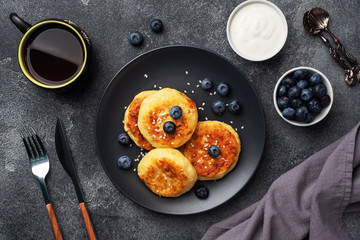 Fritters of cottage cheese with blueberries. Cheese curd cheesecakes, pancakes on a dark concrete background. Copy space.