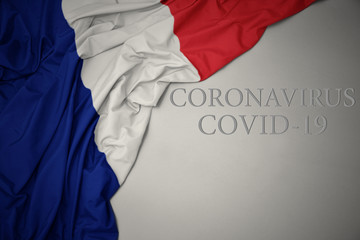 waving national flag of france with text coronavirus covid-19 on a gray background.