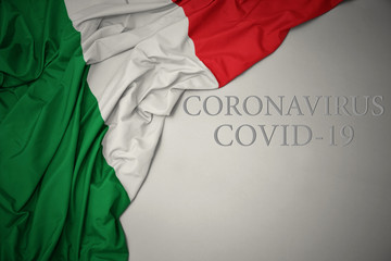 waving national flag of italy with text coronavirus covid-19 on a gray background.