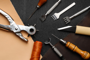 Leather crafting DIY tools lies on natural black and brown leather.