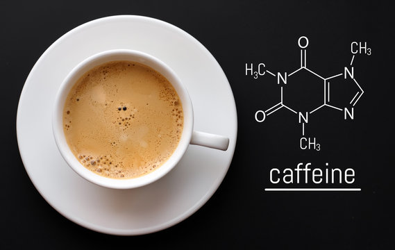 Blackboard with the chemical formula of caffeine, close up cup of fresh coffee on black background. Top view with copy space