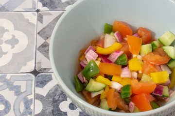Sald chopped in a green bowl with a vinegar dressing.  With tomato, onion, cucumber and peppers on a tiled surface