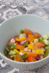 Sald chopped in a green bowl with a vinegar dressing.  With tomato, onion, cucumber and peppers on a tiled surface