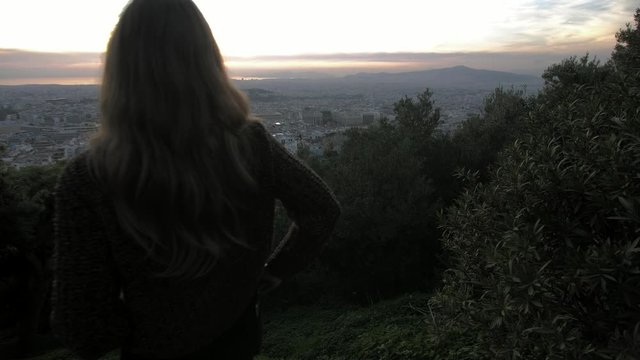 Young woman check phone and the puts it in back pocket while looking at the view of Athens from Lycabettus hill, gimbal tracks forward