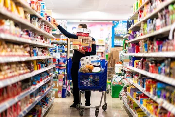 Foto op Plexiglas Full shopping cart, customer is stocking vital needs because of global chaos. Shopping with blur supermarket store products, interior background. © Sondem