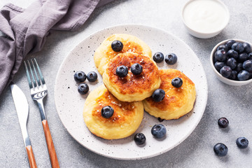Fritters of cottage cheese with blueberries. Cheese curd cheesecakes, pancakes on a grey concrete background. Copy space.