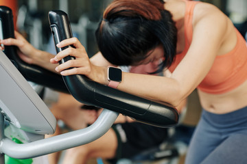 Fototapeta premium Young woman with smartwatch on wrist exhausted after training in elliptical trainer