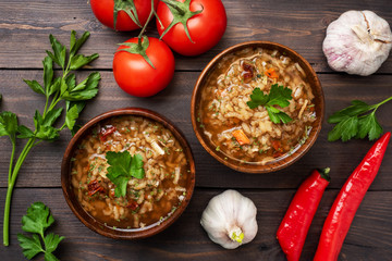 Fototapeta na wymiar Vegetarian soup kharcho with rice and vegetables. Garlic hot pepper tomatoes. Wooden rustic background, plates made of natural bamboo.