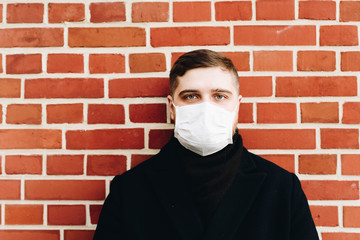 Young caucasian man with surgical mask to protect from coronavirus on a brick wall background with space for text