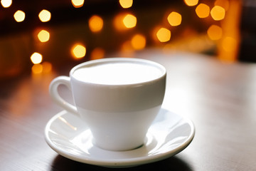 Obraz premium A cup of coffee on wooden table. Lights on the background. Front view.