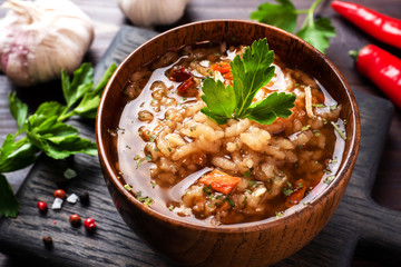 Vegetarian soup kharcho with rice and vegetables. Garlic hot pepper tomatoes. Wooden rustic background, plates made of natural bamboo.
