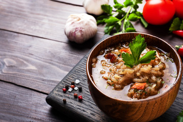 Vegetarian soup kharcho with rice and vegetables. Garlic hot pepper tomatoes. Copy space. Wooden rustic background, plates made of natural bamboo.