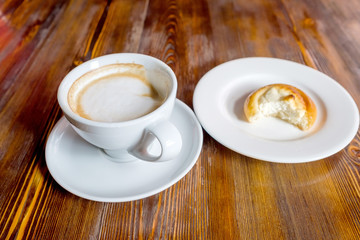 cup with coffee on a saucer next to a bitten bun