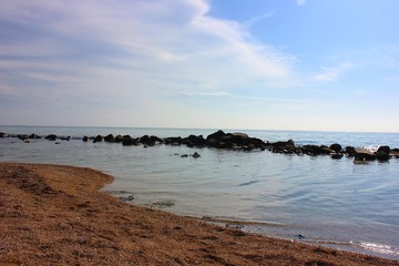 Sea and rocks. A beach with a view of the stones in the sea. Blue sea with a sandy line. Ocean horizon