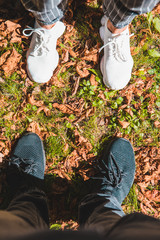 man and woman legs in black and white sneakers on green grass with red rusty leaves