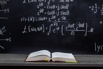 Open book on the table in classroom with blackboard background, back to school concept