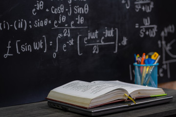 Open book on the table in classroom with blackboard background, back to school concept