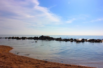 Sea and rocks. A beach with a view of the stones in the sea. Blue sea with a sandy line. Ocean horizon