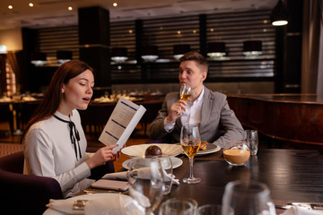caucasian couple in restaurant. young girl reads the menu, wants to make an order. handsome guy sit looking at her and waiting for her order