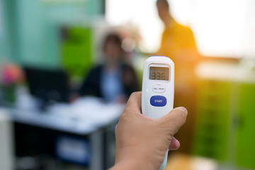Hand Holding Thermal Scanner to Check Temperature in blurred office or hospital background.