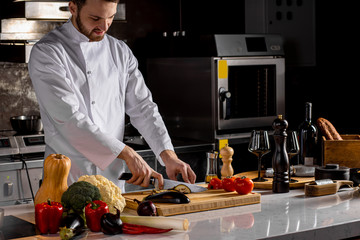 young caucasian chef-cooker cooking food in the kitchen, in restaurant. man use sharp knife and...