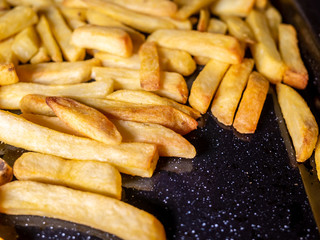  Close up and selective focus of crisp and golden oven chips on a black tray fresh from the oven