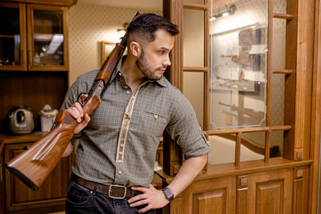 serious caucasian man stand with rifle in guns store, posing at camera, look side. man keen on...