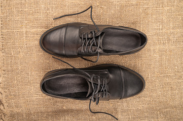 A pair of black leather boots with lacing on a background of coarse fabric. Close up.