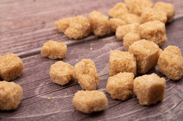 Pieces of brown sugar scattered on a wooden background. Close up.
