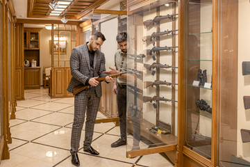 caucasian adult looking for a suitable rifle in guns store, he want to make purchase, buy rifle for...
