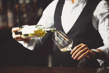 Male sommelier pouring white wine into wineglasses. - obrazy, fototapety, plakaty