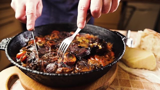 Man cuts a piece of beef, demonstrating cooked ossobuco. Traditional Italian food.