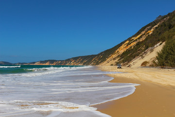 Beach along the coloured sands cliffs with rising tide and 4WD car in Rainbow Beach, Queensland, Australia