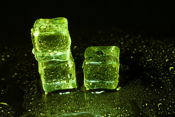Green ice cubes on black table background.