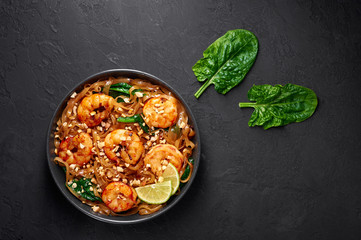 Prawn Pad See Ew in black bowl at dark slate background. Pad See Ew is thai cuisine dish with rice noodles, prawns, soy and oyster sauces and greens. Thailand food. Copy space. Top view