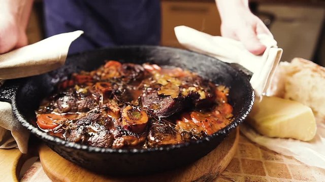 Мan puts on a table a pan with boiling ossobuco. Traditional Italian food.