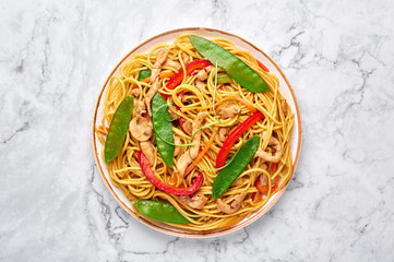 Chicken Lo Mein on white marble background. Lo Mein is Chinese cuisine dish with chicken meat, egg noodles, vegetables and sauces. Chinese Food. Stir Fried Noodles. Top view. Copy space