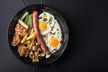 Traditional English breakfast with egg, mushrooms, cucumber and beans on a black pan background. copyspace. top view