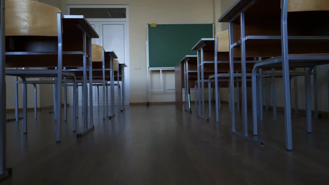 empty classroom during a break or vacation at school, university, institute, slow motion towards green blackboard, between two rows of desks
