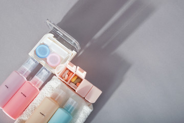 Travel kit. Set of four small plastic bottles for cosmetic products, kit for contact lenses, pill organizer, towel. Gray background with shadows.