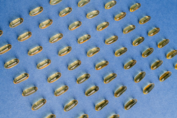 Yellow capsules with vitamin D on a blue background. Sunshine vitamin.