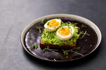 food, eating and breakfast concept - toast bread with mashed avocado, eggs and greens on ceramic plate