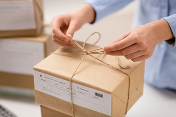 delivery, mail service, people and shipment concept - close up of woman packing parcel box and tying rope at post office