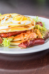 Pancakes with grilled sausages, egg, salad drizzled with sauce on a white plate