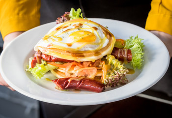 Pancakes with grilled sausages, egg, salad drizzled with sauce on a white plate. Plate with pancakes in hands