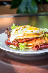 Pancakes with grilled sausages, egg, salad drizzled with sauce on a white plate