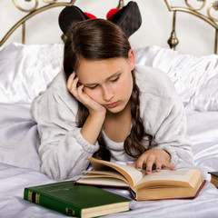 sad young student girl reads a book while lying on a bed doing homework