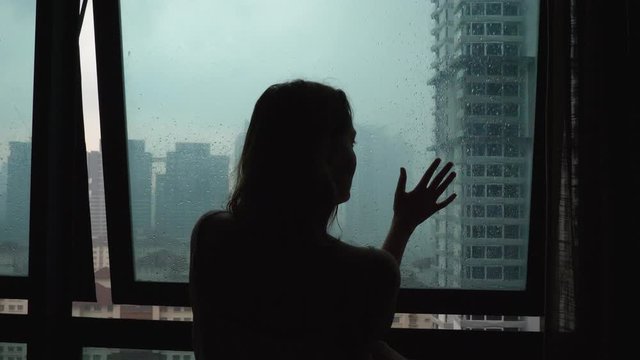 Silhouette sad loneliness woman touch glass window at rain day on city view background