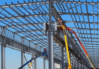 Workers on aerial work platforms build the metal structure of the roof of a large building. © luca piccini basile